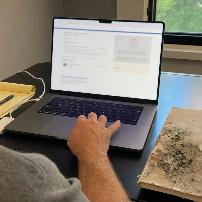 A homeowner checks a credential beside a mold stained drywall sample.